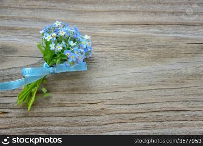 Small bouquet of blue forget-me-not flowers, tied a blue ribbon, on the background of old wooden plank