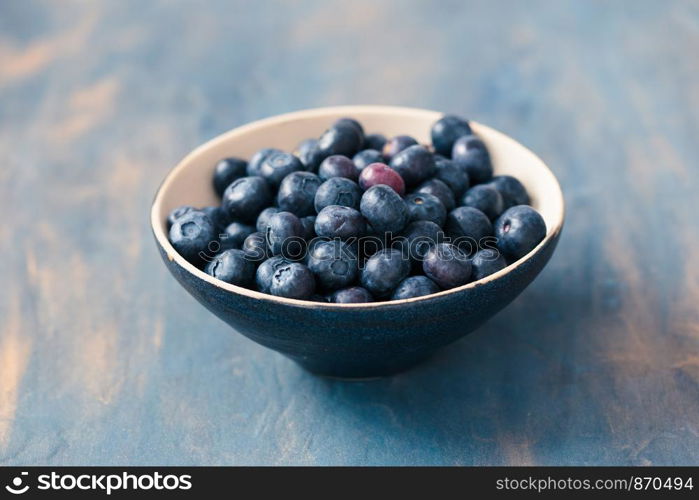 Small bowl full of fresh blueberries put on table painted in blue