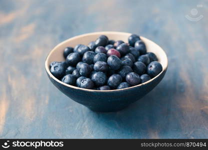 Small bowl full of fresh blueberries put on table painted in blue