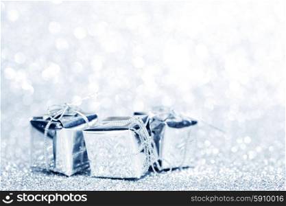 Small boxes with decorative holiday gifts on silver bokeh background