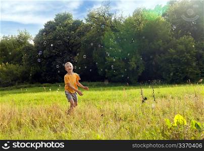 Small boy catching soap bubbles in the green field