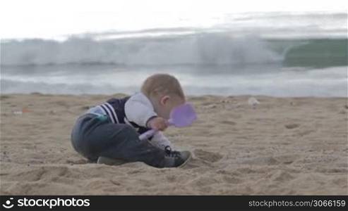 Small boy is playing with shovel and sand at the beach in summer