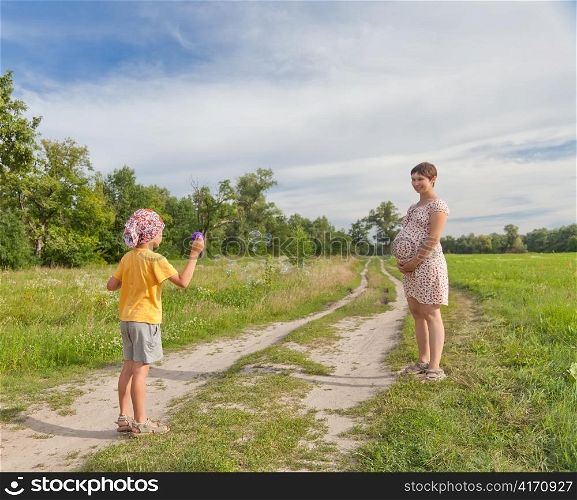Small boy making soap bubbles with his regnant mother in the green field