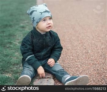 Small boy sits on ground and looks away in the autumn