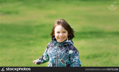 Small boy smiling and running on the background of green field, wide angle