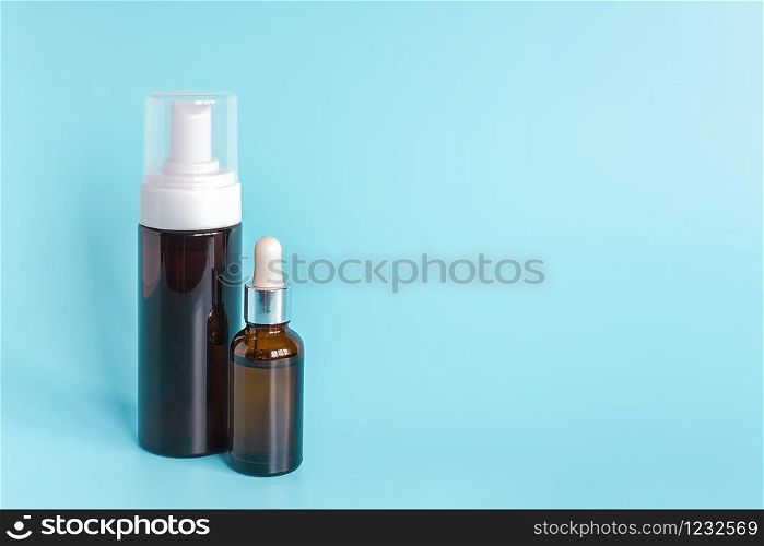 Small brown dropper bottle and big bottle with white dispenser on blue background. Concept beauty cosmetics product.. Small brown dropper bottle and big bottle with white dispenser on blue background. Concept beauty cosmetics product