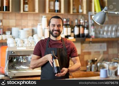 small business, alcohol drinks, people and service concept - happy man or waiter with bottle of red wine at bar. happy man or waiter with bottle of red wine at bar