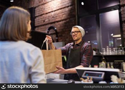 small business, food, people and service concept - happy female customer taking paper bag from man or barman at vegan cafe. woman taking paper bag from seller at cafe