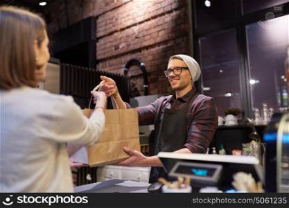 small business, food, people and service concept - happy female customer taking paper bag from man or barman at vegan cafe. woman taking paper bag from seller at cafe