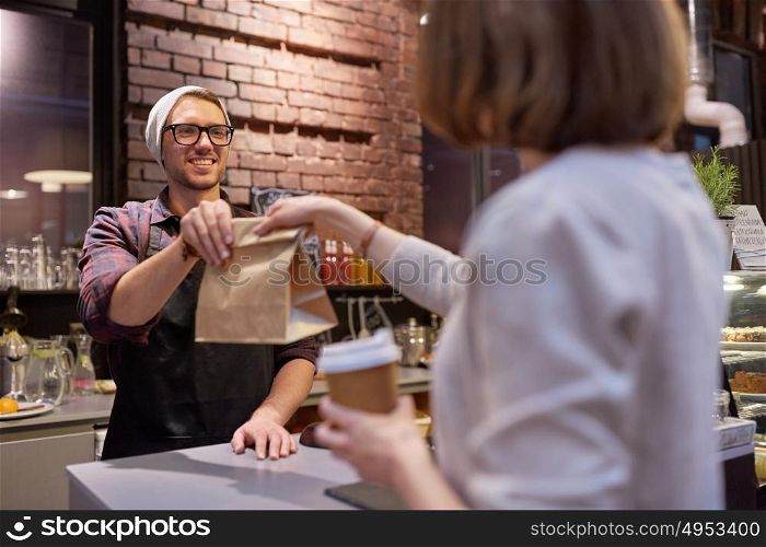 small business, food, people and service concept - happy female customer with coffee cup taking paper bag from man or barman at vegan cafe. woman taking paper bag from seller at cafe