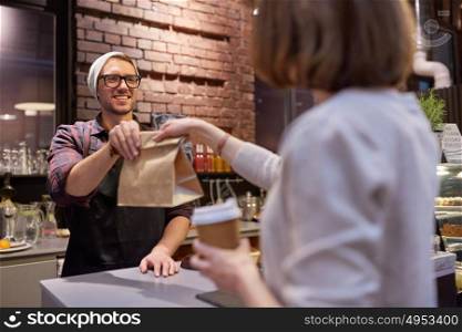 small business, food, people and service concept - happy female customer with coffee cup taking paper bag from man or barman at vegan cafe. woman taking paper bag from seller at cafe