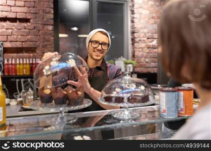 small business, food, people and service concept - happy man or barman with cakes serving female customer at vegan cafe. man or barman with cakes serving customer at cafe