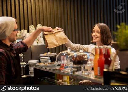 small business, food, people and service concept - happy man or barman giving paper bag to female customer at vegan cafe. man or barman giving paper bag to customer at cafe