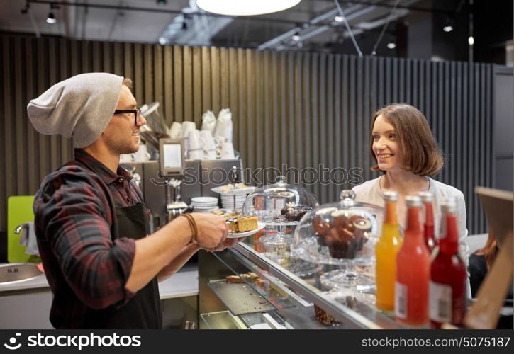 small business, food, people and service concept - happy man or barman with cake serving female customer at vegan cafe. man or barman with cake serving customer at cafe