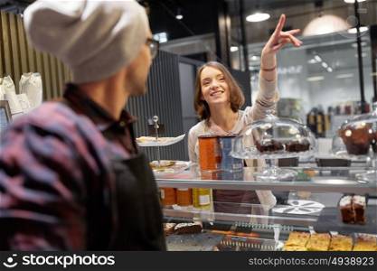 small business, food, people and service concept - happy woman showing something to seller or bartender at vegan cafe. happy woman showing something to bartender at cafe