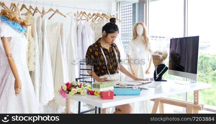 Small Business of Asian women Fashion Designer Working and using smart phone and tablet With Wedding Dresses at at clothing store