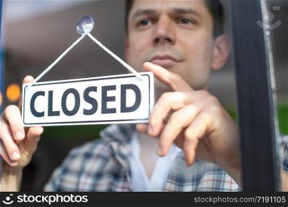 Small Business Owner With Serious Expression Putting Up Closed Sign During Recession Or Health Pandemic
