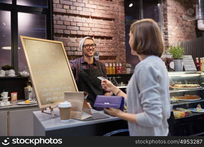 small business, payment, people and service concept - happy barman and woman paying with credit card at cafe. barman and woman paying with credit card at cafe