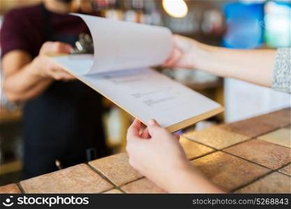 small business, people and service concept - bartender showing menu to customer at bar or coffee shop. bartender showing menu to customer at bar