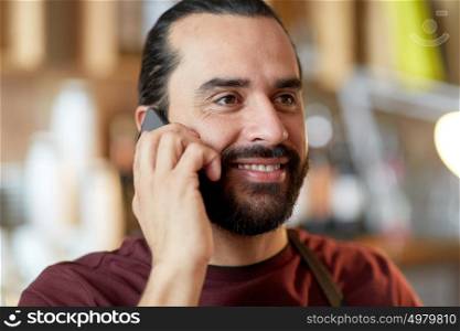 small business, people and service concept - close up of happy man or waiter in apron calling on smartphone at bar. close up of man or waiter calling on smartphone
