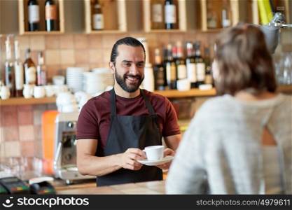 small business, people and service concept - happy man or waiter giving cup with hot drink to customer at coffee shop or bar. man or waiter serving customer in coffee shop