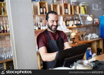 small business, people and service concept - happy man or waiter in apron at counter with cashbox working at bar or coffee shop. happy man or waiter at bar cashbox