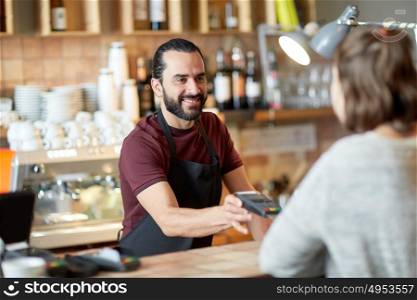 small business, people and service concept - happy man or waiter in apron with card reader and customer paying at bar of coffee shop. man or waiter with card reader and customer at bar
