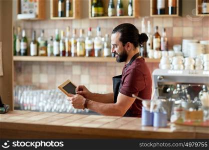 small business, people and service concept - happy man or waiter in apron with black chalkboard banner at bar or coffee shop. happy man or waiter with chalkboard banner at bar