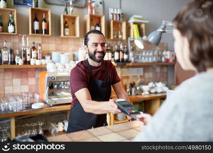 small business, people and service concept - happy man or waiter in apron with card reader and customer paying at bar of coffee shop. man or waiter with card reader and customer at bar