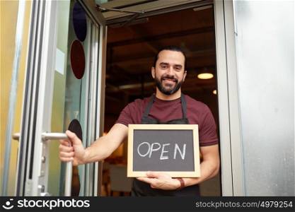 small business, people and service concept - happy man or waiter with open word on blackboard at bar or restaurant entrance door. man or waiter with blackboard at bar entrance door