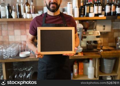 small business, people and service concept - happy man or waiter with blank blackboard at bar. happy man or waiter with blank blackboard at bar
