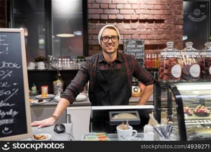 small business, people and service concept - happy seller man or barman at counter with cashbox in vegan cafe or coffee shop. happy seller man or barman at cafe counter
