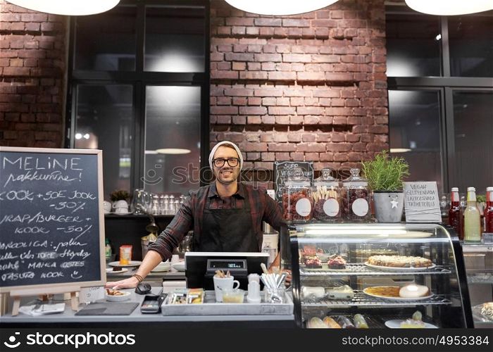 small business, people and service concept - happy seller man or barman at counter with cashbox in vegan cafe or coffee shop. happy seller man or barman at cafe counter
