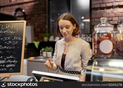 small business, people and service concept - happy woman or barmaid at counter with cashbox working in cafe or coffee shop. happy woman or barmaid with cashbox at cafe