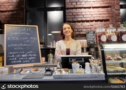 small business, people and service concept - happy woman or barmaid at counter with cashbox in cafe or coffee shop. happy woman or barmaid at cafe counter