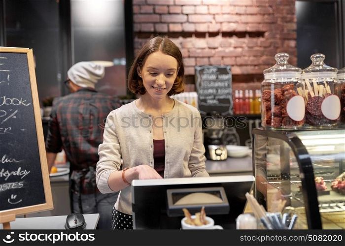 small business, people and service concept - happy woman or barmaid at counter with cashbox working in cafe or coffee shop. happy woman or barmaid with cashbox at cafe