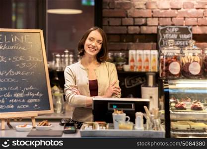 small business, people and service concept - happy woman or barmaid at counter with cashbox in cafe or coffee shop. happy woman or barmaid at cafe counter. happy woman or barmaid at cafe counter