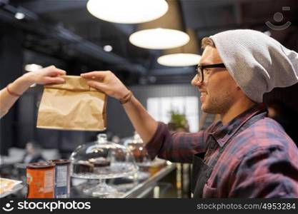 small business, people and service concept - man seller giving paper bag to customer at cafe. man seller giving paper bag to customer at cafe
