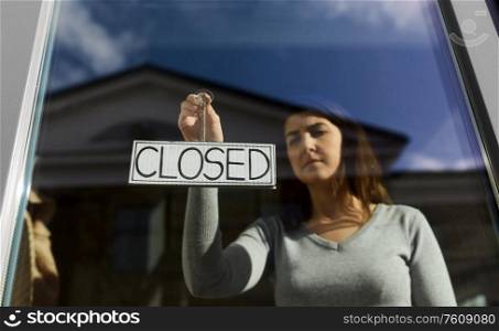 small business, people and service concept - young woman hanging banner with closed word on door or window. woman hanging banner with closed word on door