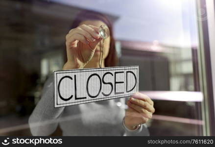 small business, people and service concept - young woman hanging banner with closed word on door or window. woman hanging banner with closed word on door