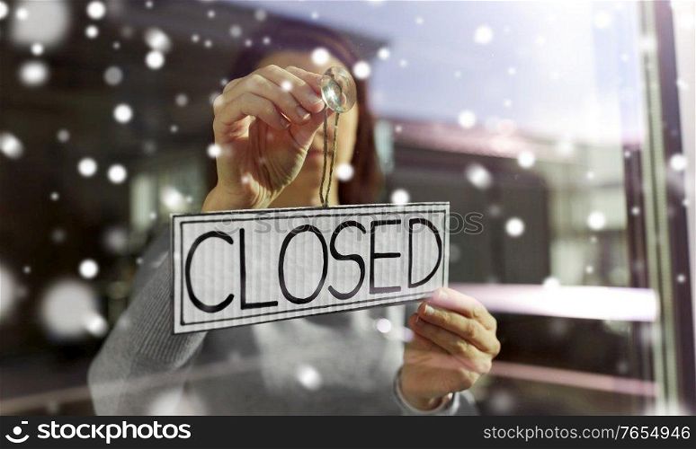 small business, people and service concept - young woman hanging banner with closed word on door or window in winter over snow. woman hanging banner with closed word on door