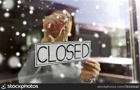 small business, people and service concept - young woman hanging banner with closed word on door or window in winter over snow. woman hanging banner with closed word on door