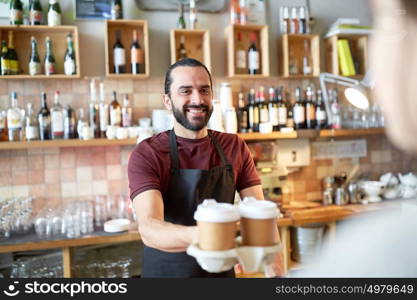 small business, people, takeaway and service concept - happy man or waiter giving paper cup with hot drink to customer at coffee shop. man or waiter serving customer in coffee shop