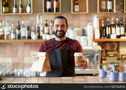 small business, people, takeaway and service concept - happy man or waiter in apron holding coffee cups and paper bag at bar. man or waiter with coffee and paper bag at bar