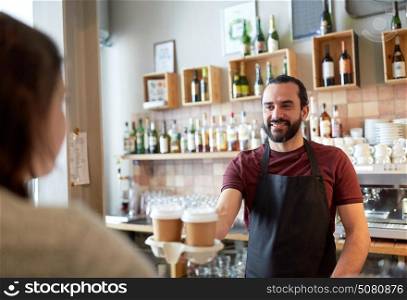 small business, people, takeaway and service concept - happy man or waiter giving paper cup with hot drink to customer at coffee shop. man or waiter serving customer in coffee shop