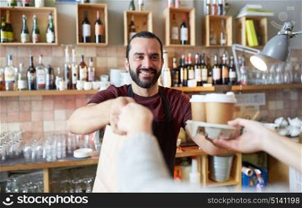 small business, people, takeaway and service concept - happy man or waiter giving bag and paper cups with hot drinks to customer at coffee shop. man or waiter serving customer at coffee shop