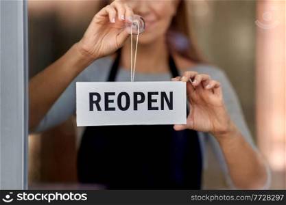 small business, reopening and service concept - happy smiling woman hanging reopen banner on window or door glass. happy woman hanging reopen banner on door glass