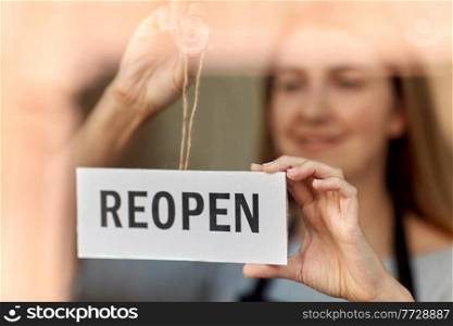 small business, reopening and service concept - happy smiling woman hanging reopen banner on window or door glass. happy woman hanging reopen banner on door glass