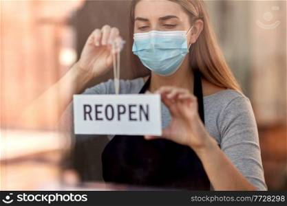 small business, reopening and service concept - woman in mask hanging reopen banner on window or door glass. woman in mask with reopen banner on door glass