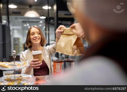 small business, takeaway food, people and service concept - happy female customer with coffee cup taking paper bag from man or barman at vegan cafe. woman taking paper bag from seller at cafe